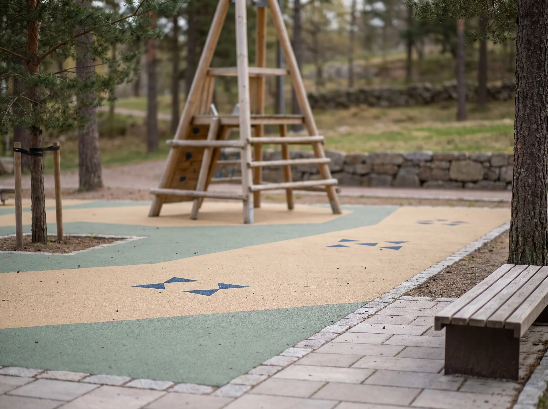 Lekplats med träkonstruktion och färgglatt gummigolv i naturmiljö.